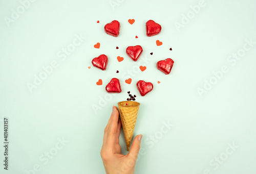 A woman hand holds a waffle horn in her hand with red hearts sweets explosing from the horn like a firework photo