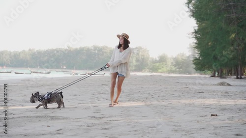The young asian woman lead 2 puppy french bulldogs at the beach in sunny day in slow motion