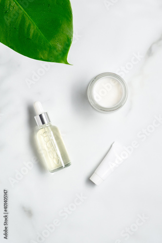 Natural organic cosmetics set. Serum lotion in glass dropper bottle, moisturizer, tube with cream on marble table. Flat lay, top view.