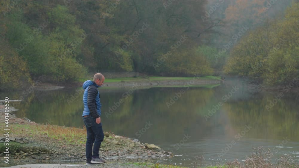 A man in a blue jacket throwing stones at the Urrunaga swamp in Álava, Spain - Medium shot A man in a blue jacket throwing stones at the Urrunaga swamp in Álava, Spain - Medium shot