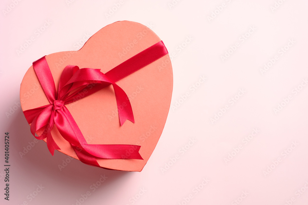 Heart shaped box with red ribbon bow on pink background, top view. Happy Valentines day greeting card template.