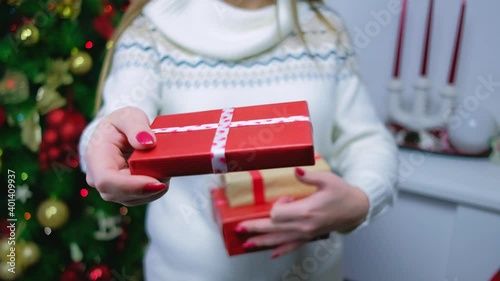 A girl near a Christmas tree and a fireplace with gifts in her hands chooses one to show it to in focus. New Year's gifts for Christmas