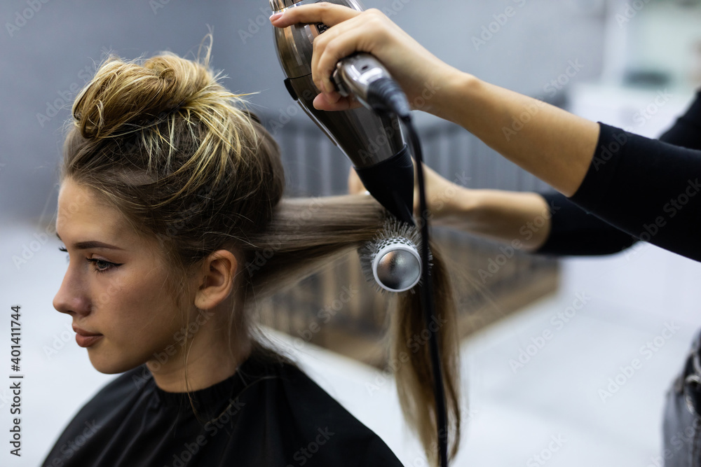Naklejka premium Young hairdresser using hair dryer and comb to the hair of woman