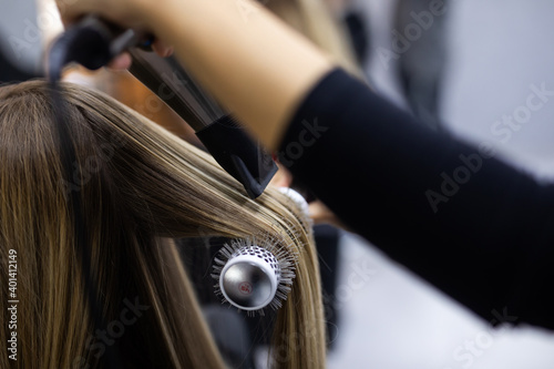 Professional woman hairdresser drying woman's hair styling using blow dryer at the hairdressing saloon