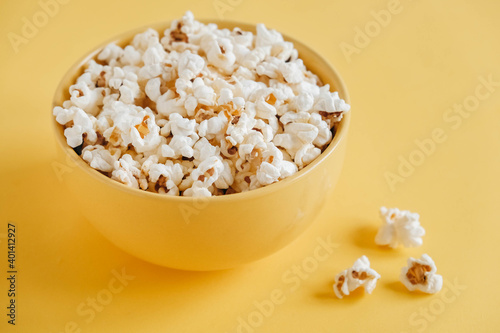 Popcorn in a yellow bowl on a yellow background. Top view. Copy, empty space for text