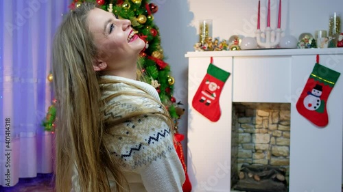 the girl sitting against the background of the christmas tree and by the fireplace in the mask takes off the mask emotion 2021 without covid 19