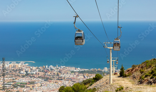 A cable car on the Mediterranean coast in Andalusia. It leads to the Calamorro mountain. It is a summer day with blue skies and sunshine. Below is the city with the harbor.