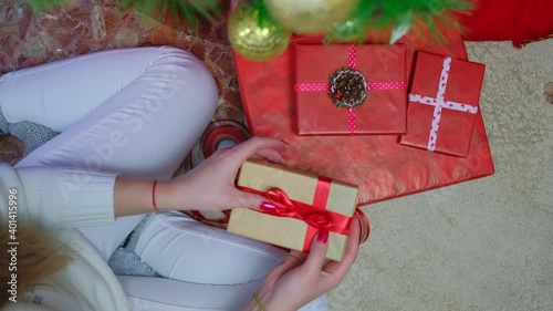 A girl in a white sweater sits at home by a Christmas tree and packs a box with a gift. Top view