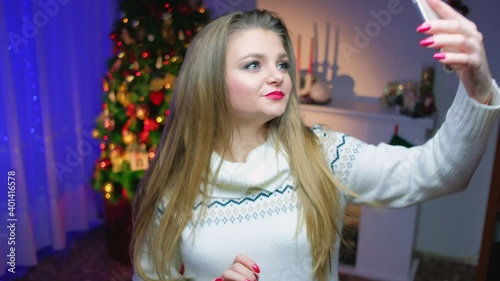 girl posing looking at the front camera of the phone christmas tree and fireplace on the background