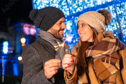 Winter portrait of a Caucasian couple enjoying the Christmas lights with torches in hand, lifestyle