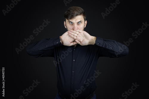a man in a black shirt and on a black background covered his mouth with his hands © Roman
