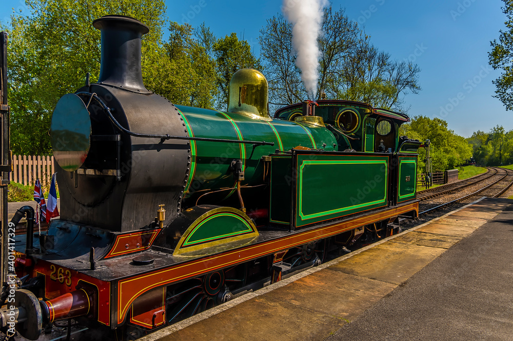 Fototapeta premium A train letting off steam before moving off on a railway line in the UK on a sunny summer day