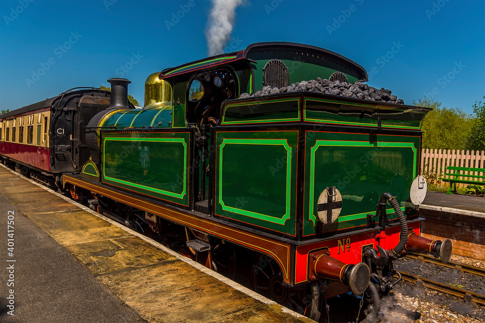 Obraz premium A train at a station letting off steam on a railway line in Sussex, UK on a sunny summer day