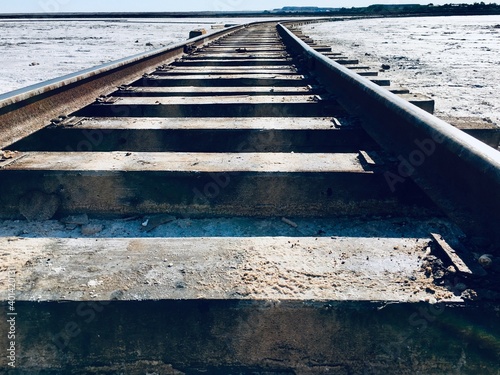 sleepers and rails run along the ground that is covered with white salt