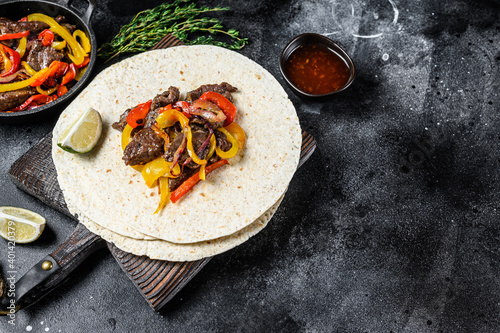Mexican Fajitas with colored pepper and onions, served with tortillas and salsa. Black background. Top view. Copy space