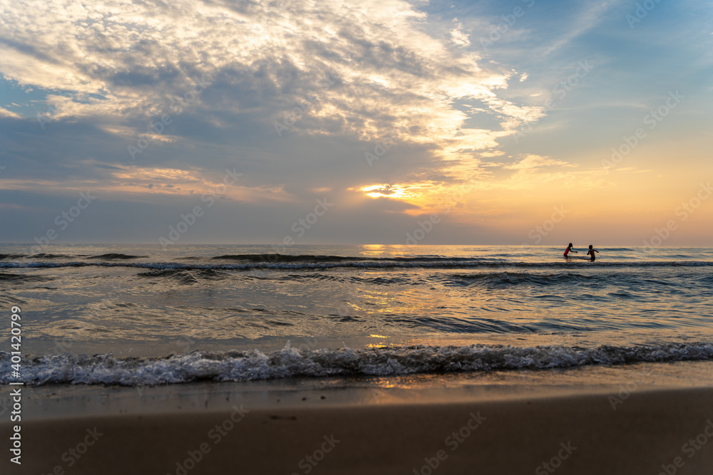 Children playing in the waves at the beach at sunset