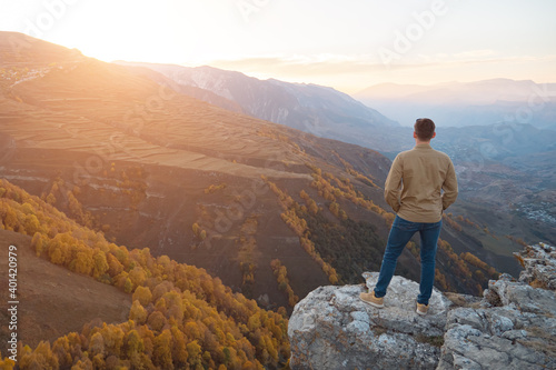 Canvas-taulu Man in shirt admires sunrise over mountains with coloured forests and fields sta