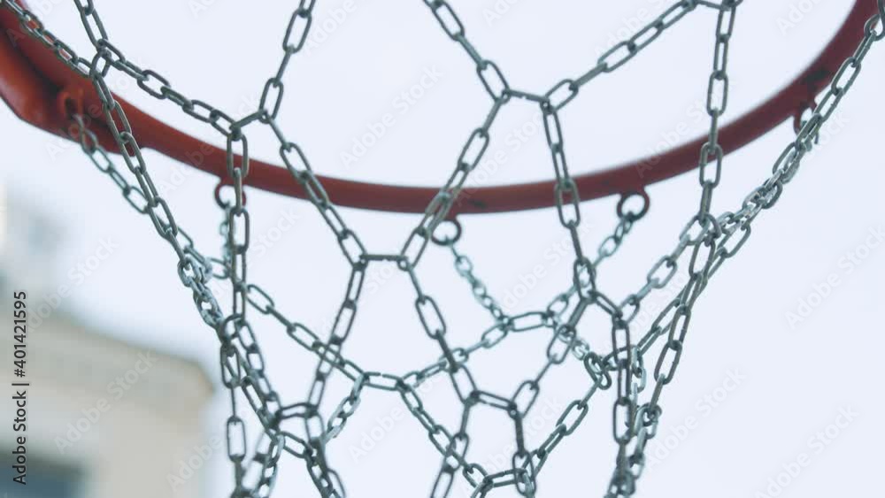Basketball hoop with metal net outdoors. Orange ball flying in ring. Score in outdoor competitive game. Basketball hoop with metal net outdoors. Orange ball flying in ring. Score in outdoor competitive game.
