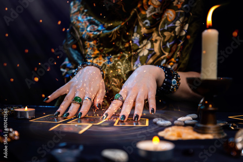 Cartomancy. A fortune teller reads Tarot cards. On the table are candles and fortune-telling objects and sparks. Hands close up. The concept of divination, astrology and esotericism