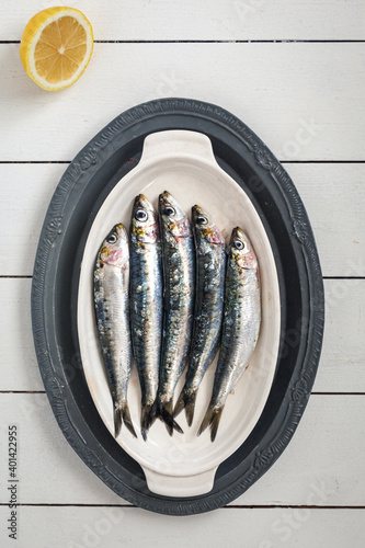 A high angle photo of fresh, raw sardines on a white plate and white background with lemon photo