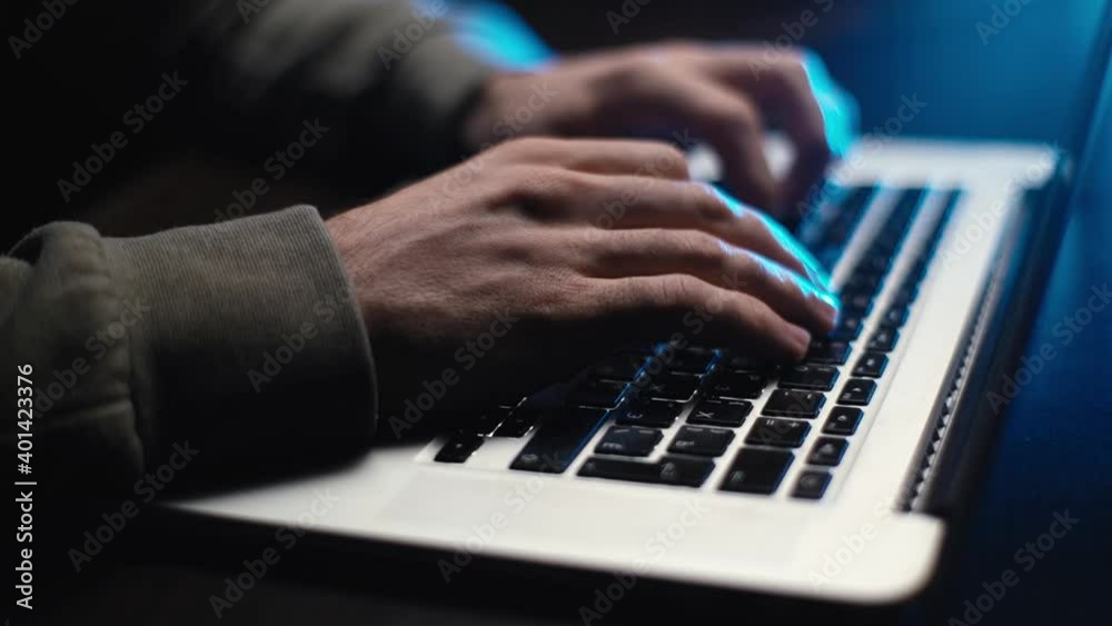 Extreme close-up hands of unrecognizable hacker programmer working typing on keyboard laptop computer at dark room. Businessman working typing on keyboard laptop computer from home, soft blue color. Extreme close-up hands of unrecognizable hacker programmer working typing on keyboard laptop computer at dark room. Businessman working typing on keyboard laptop computer from home, soft blue color.