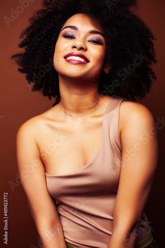 pretty young african american woman with curly hair posing cheerful gesturing on brown background, lifestyle people concept