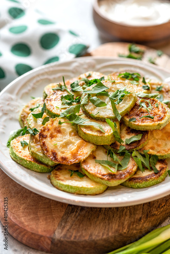 Fried zucchini with parsley, garlic, and sauce in a white ceramic plate close-up. Vegetarian snack.