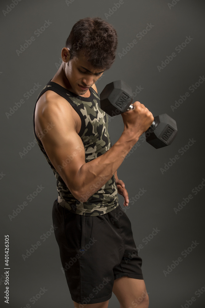 muscular young man lifting weights for biceps curl on dark background.