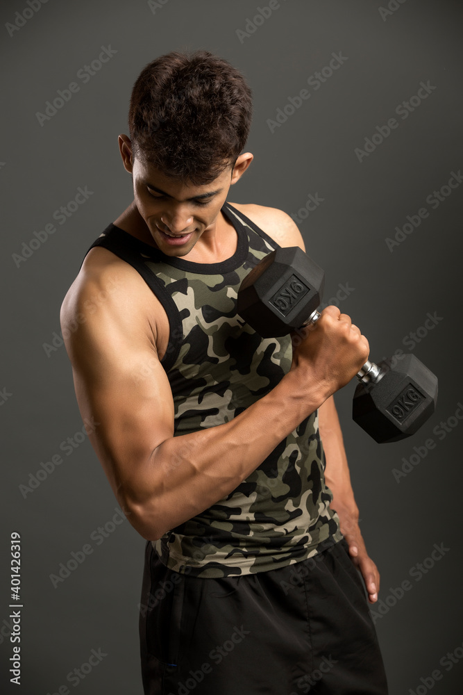 muscular young man lifting weights for biceps curl on dark background.