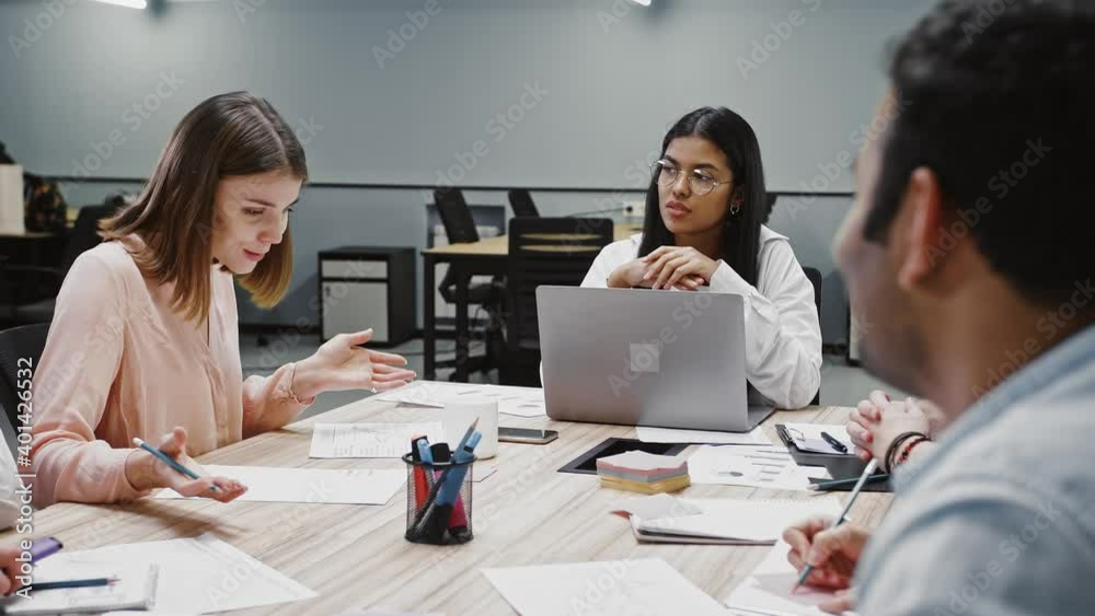 Female boss discussing business ideas with team of diverse colleagues during brainstorming, sitting at table in office Female boss discussing business ideas with team of diverse colleagues during brainstorming, sitting at table in office