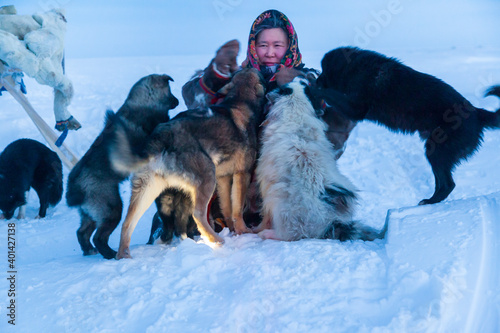 A woman, in the national winter clothes of the northern inhabitants of the tundra, plays with a dogs in minus 40, in the polar night