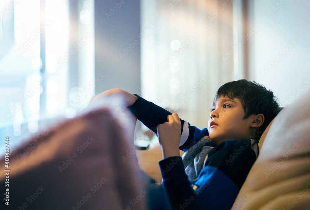 Cinematic portrait young boy siting on sofa watching TV, Candid shot