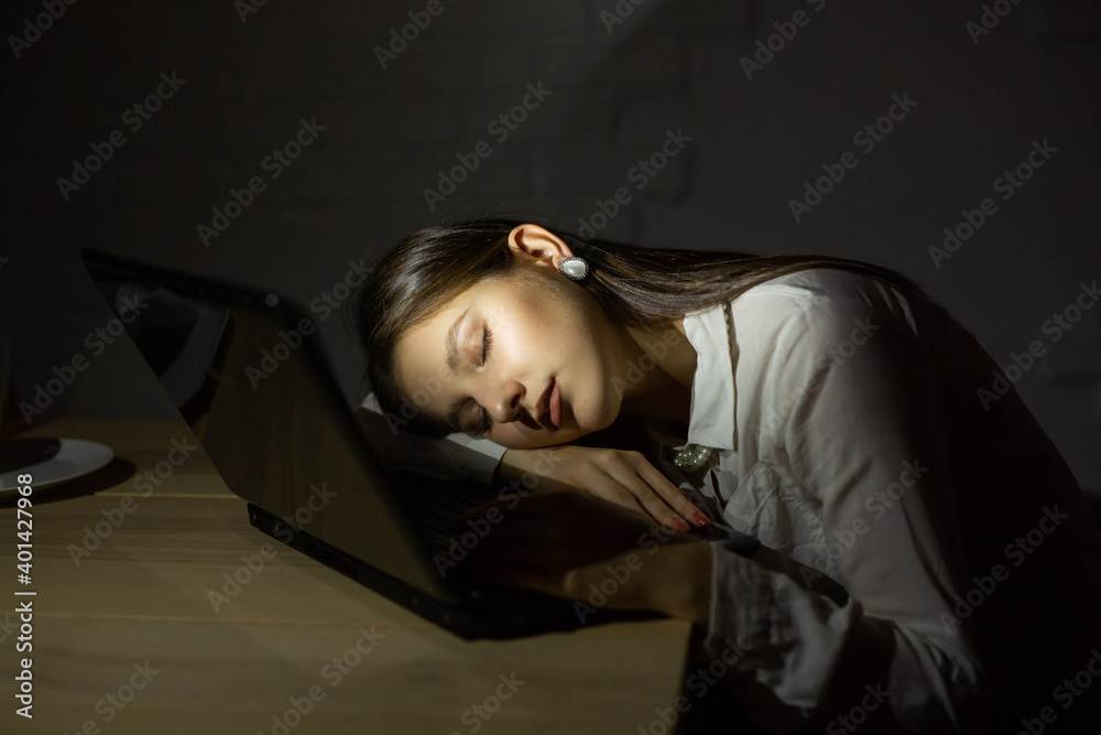 beautiful young female sleeping at night behind a laptop