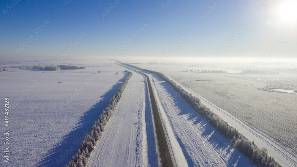 Winter road along the fields between cities aerial view from a drone. Winter road view from a drone Winter road along the fields between cities aerial view from a drone. Winter road view from a drone