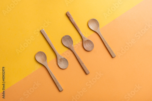 Group of five empty wooden spoons on orange and yellow background, top view with copy space. Zero waste, eco-friendly kitchen utensils made of bamboo, sustainable lifestyle concept