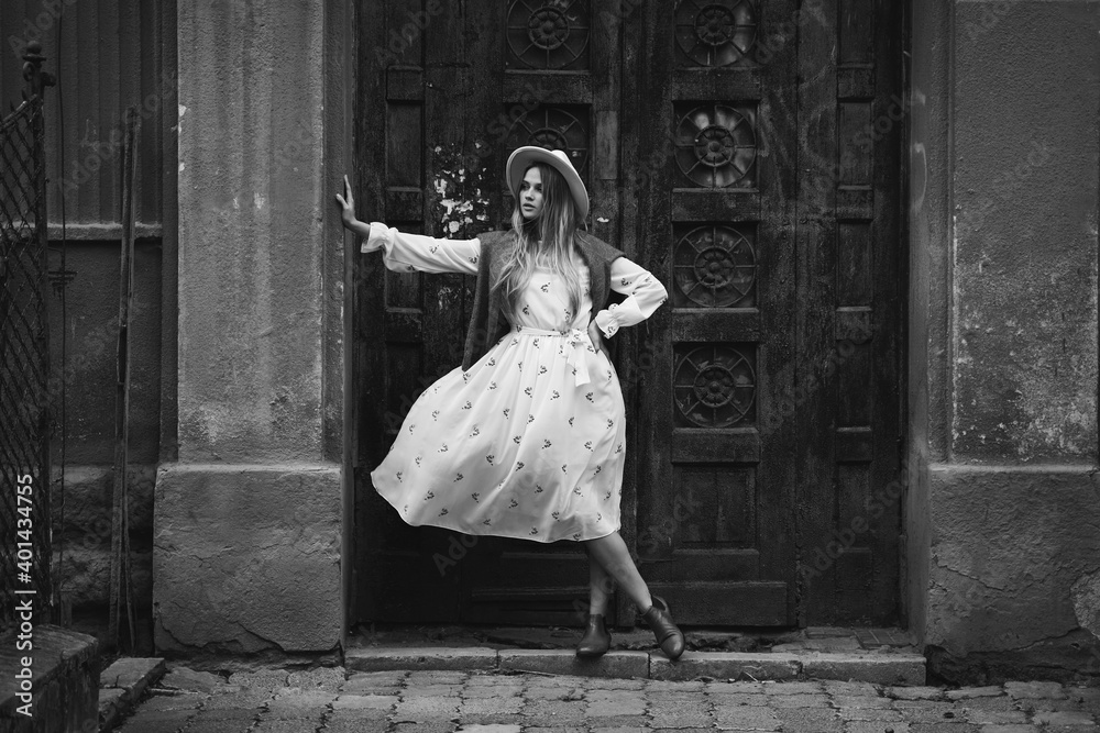 Young beautiful fashionable model in hat in old city. White dress waving in wind. Black and white portrait. Young beautiful fashionable model in hat in old city. White dress waving in wind. Black and white portrait.