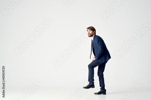 business man in a blue suit stands on one leg on a light background side view © SHOTPRIME STUDIO