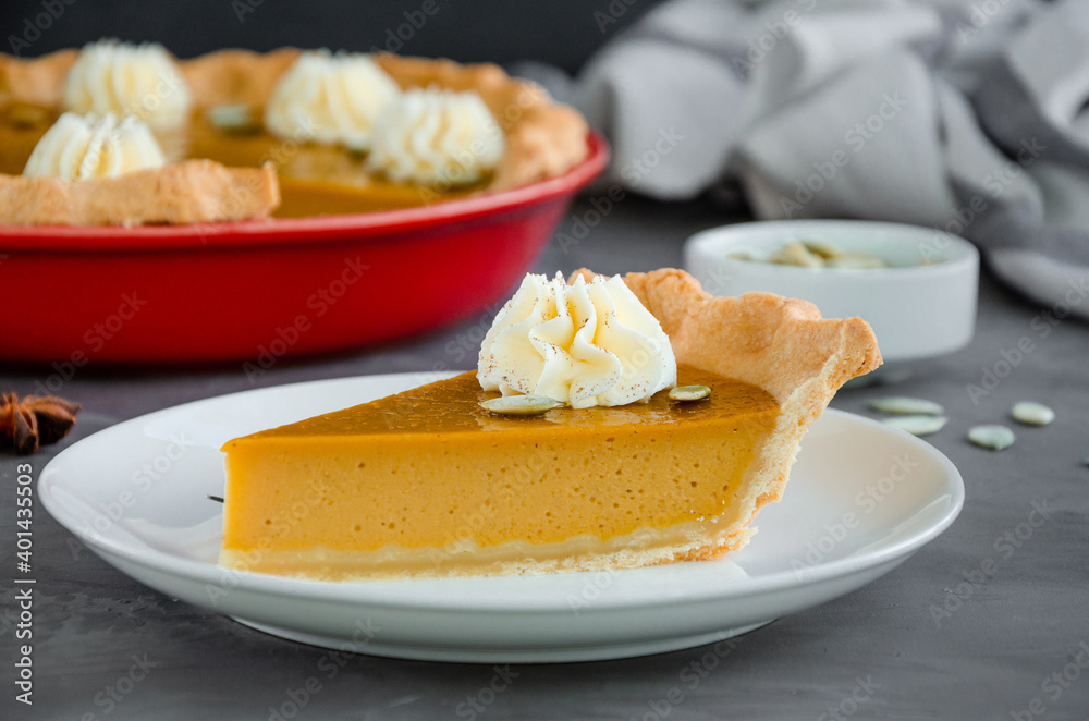 Traditional festive pumpkin pie with spices, whipped cream and seeds on top on a dark stone background. Dessert for Thanksgiving. Traditional festive pumpkin pie with spices, whipped cream and seeds on top on a dark stone background. Dessert for Thanksgiving.