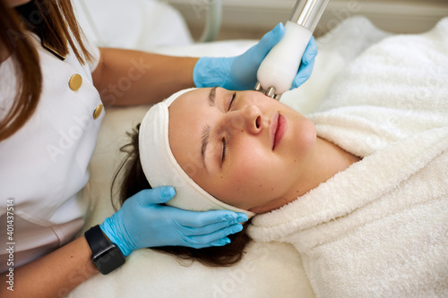 Tablou pe pânză Beautiful woman receiving facial microcurrent procedure for lifting and rejuvenation skin