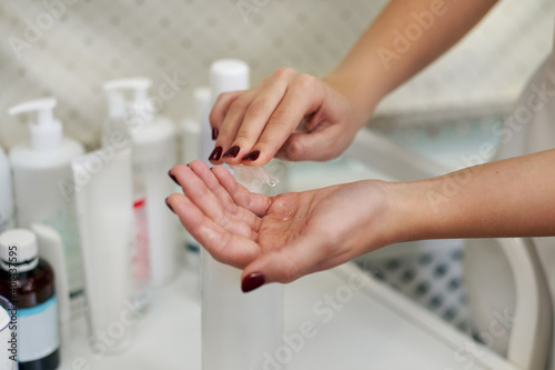 Focus on beautician's hands while applying disinfectant gel to hands using a dispenser