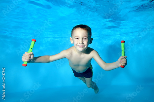 Portrait of a beautiful boy at the bottom of a children's pool. He smiles and looks into the camera frame. Fun dives underwater. Active happy child. Swimming classes. Bodily exercises photo