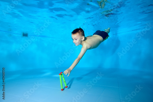 Cute athletic boy dives to the bottom of the pool for a toy. Fun dives underwater. Active happy child. Swimming classes. Bodily exercises. Healthy lifestyle