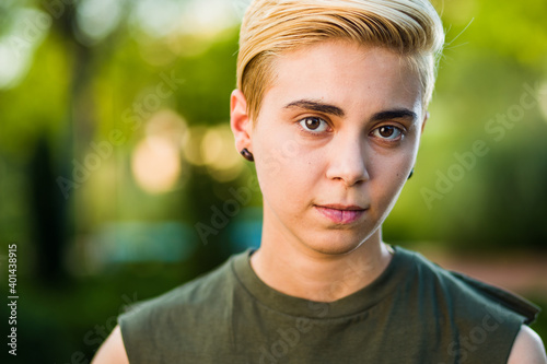 Young woman beauty Tomboy lifestyle with blonde short hair posing in casual clothes in a park in Spain.
Jeans and t-shirt showing armes, gender education and non binary teen.