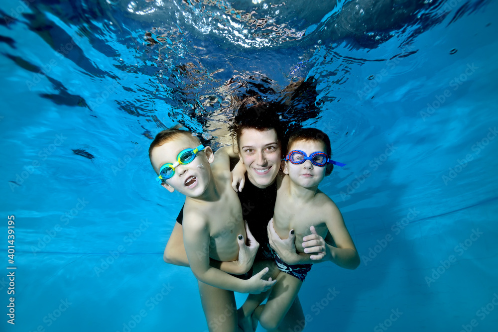 Two beautiful boys underwater with their mother. She hugs them tenderly. They smile and look at the camera. Active happy children. Healthy lifestyle. Swimming lessons under the water. Family sports