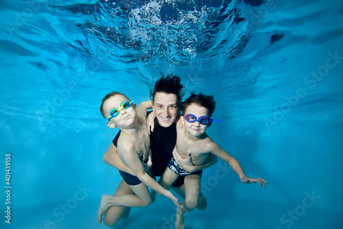 Two little boys swim under the water with their mother. She hugs them tenderly. Active happy children. Healthy lifestyle. Swimming lessons under the water. Family sports