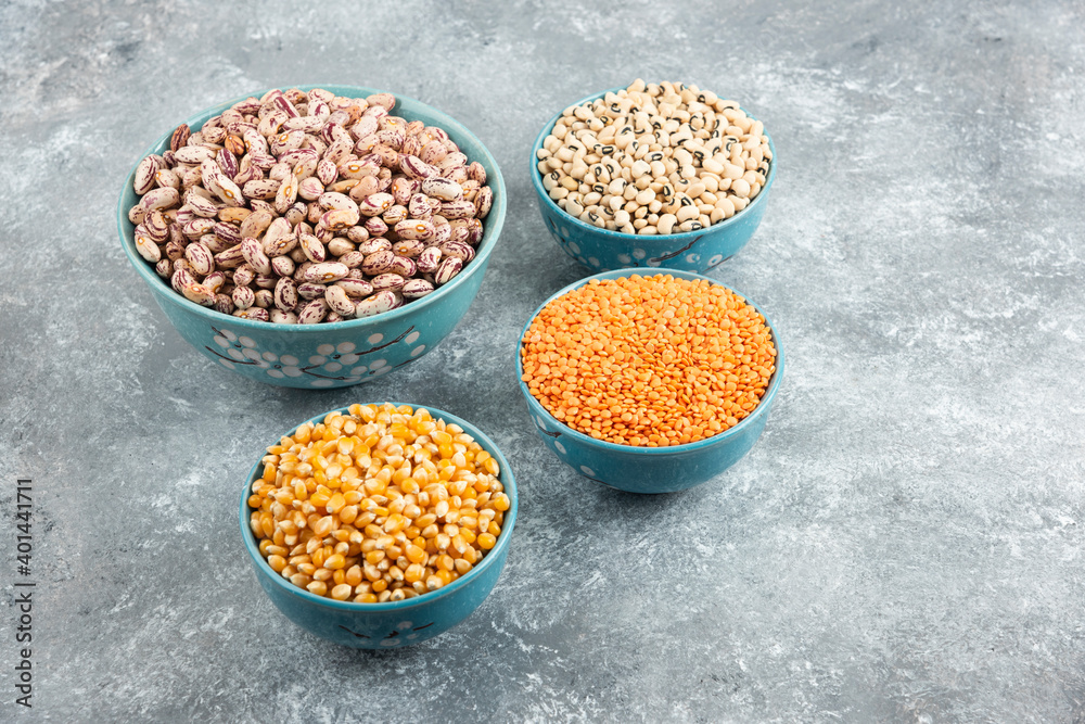 Bowls of raw beans, lentils and corns on marble surface