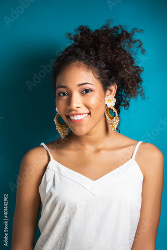 mujer latina morena con cabello crespo rizado sonriendo mirando la camara en un fondo azul