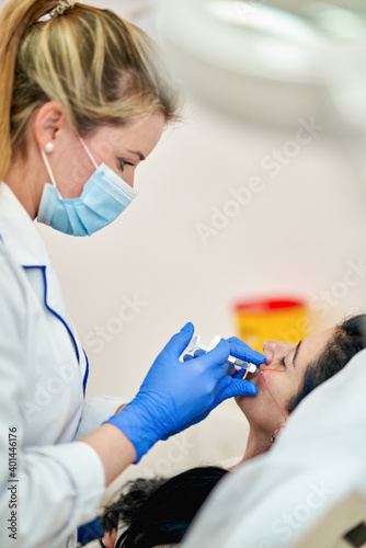 close up of hands of cosmetologist making botox injection. She is holding syringe. Woman is receiving procedure with enjoyment.