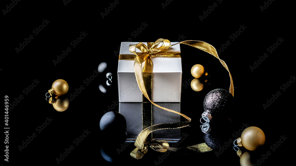 Christmas gift. White gift with golden bow, gold balls and new year tree in xmas decoration on dark background for greeting card. Winter festive composition with copy space.