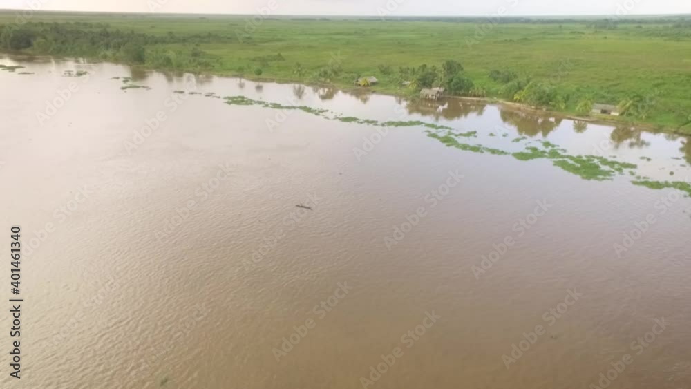 Aerial view of a tiny indigenous canoe cruising the Orinoco River with small indigenous houses at the shore Aerial view of a tiny indigenous canoe cruising the Orinoco River with small indigenous houses at the shore